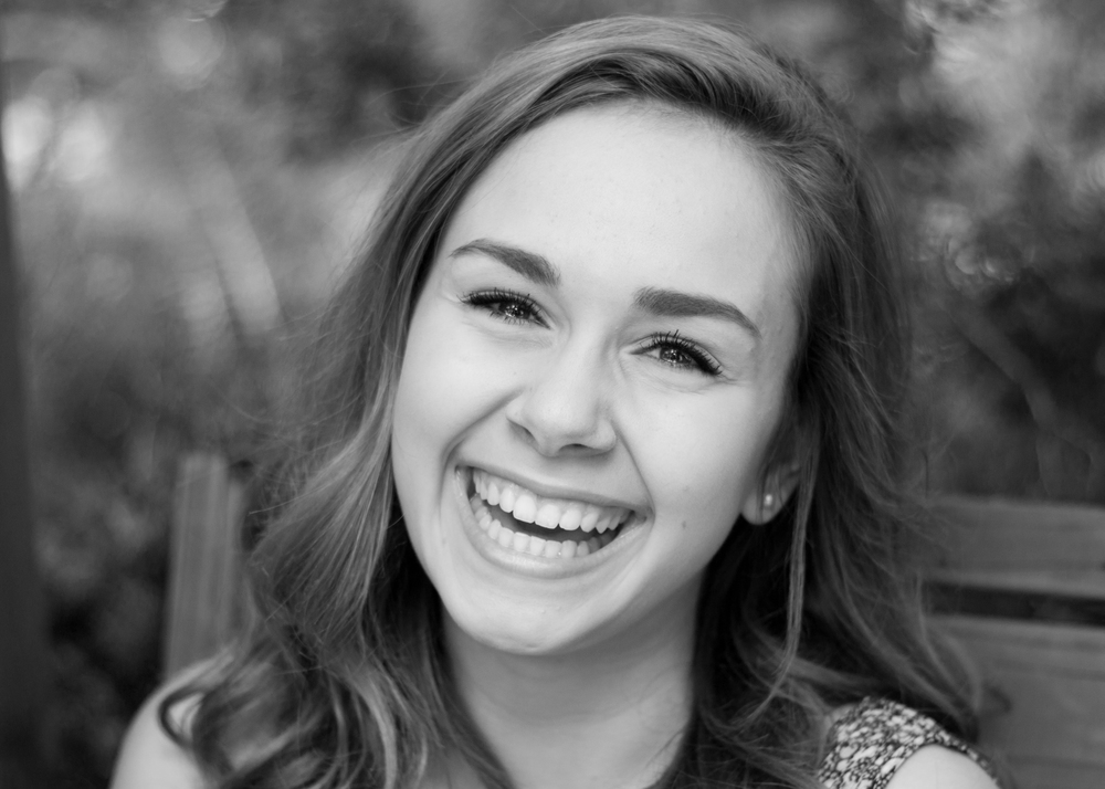 A young woman with long hair laughs and looks into the camera.