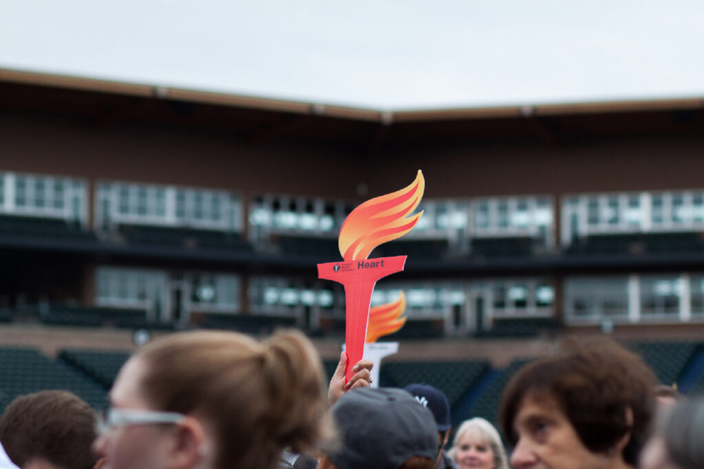 In a crowd, a person holds up a paper torch for the American Heart Association.
