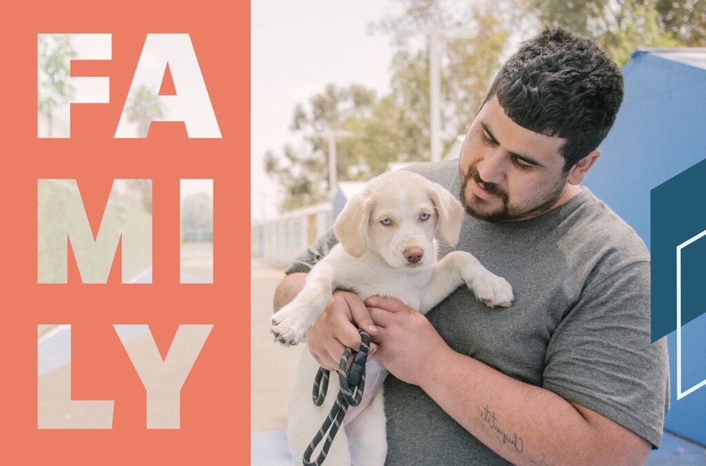 A man holds a tiny puppy in front of a temporary shelter, with "FAMILY" written over the image.
