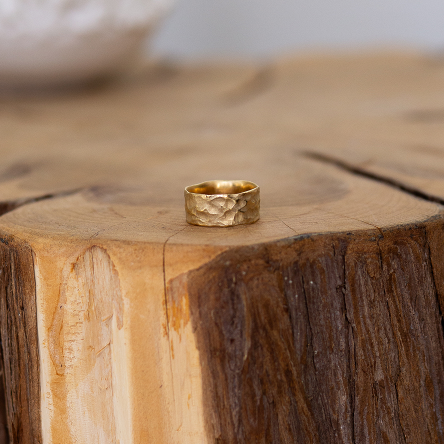 A gold band engagement ring with an ocean wave texture.