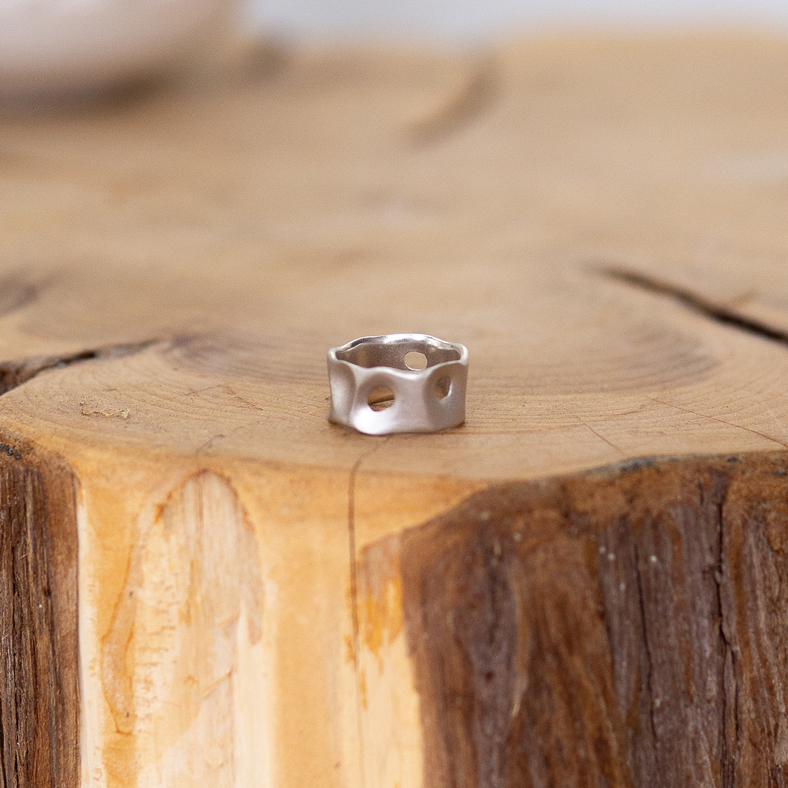 A silver banded wedding ring with holes punched out, representing pebbles.