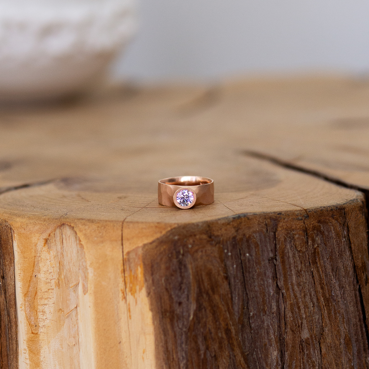 A rose gold banded ring with a center diamond sits on a log table.